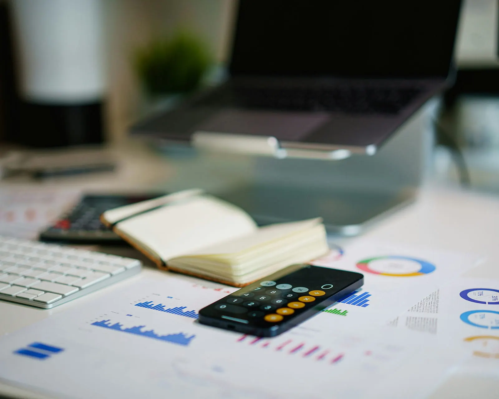A desk with budget charts, a notebook, and a phone calculator app