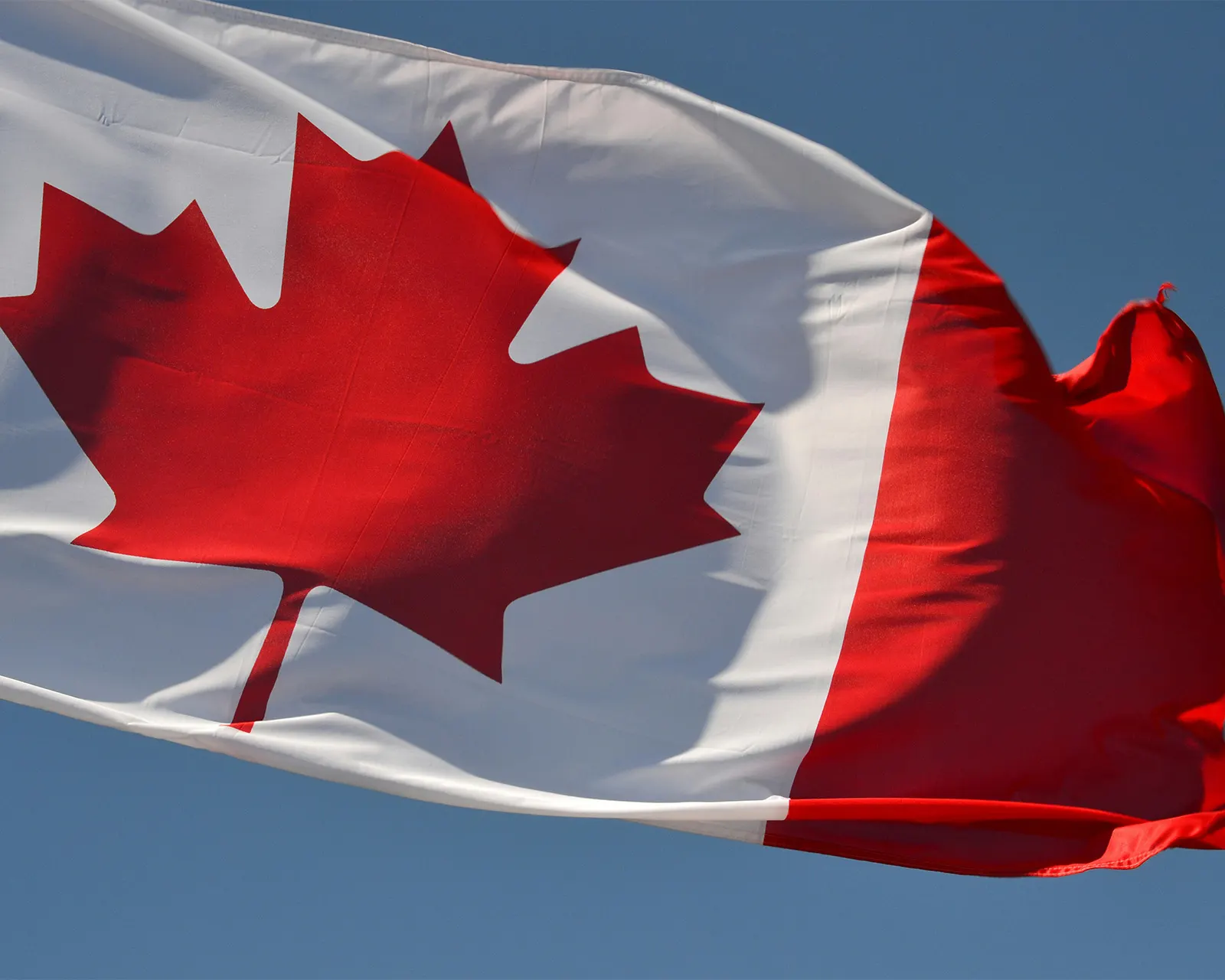 A Canadian flag waving against a blue sky